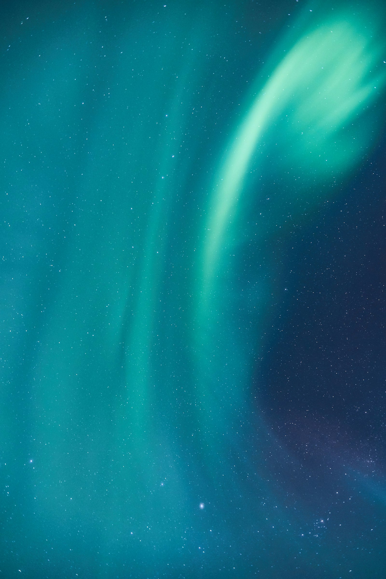 Aurora in green and teal sweeping across a field of stars