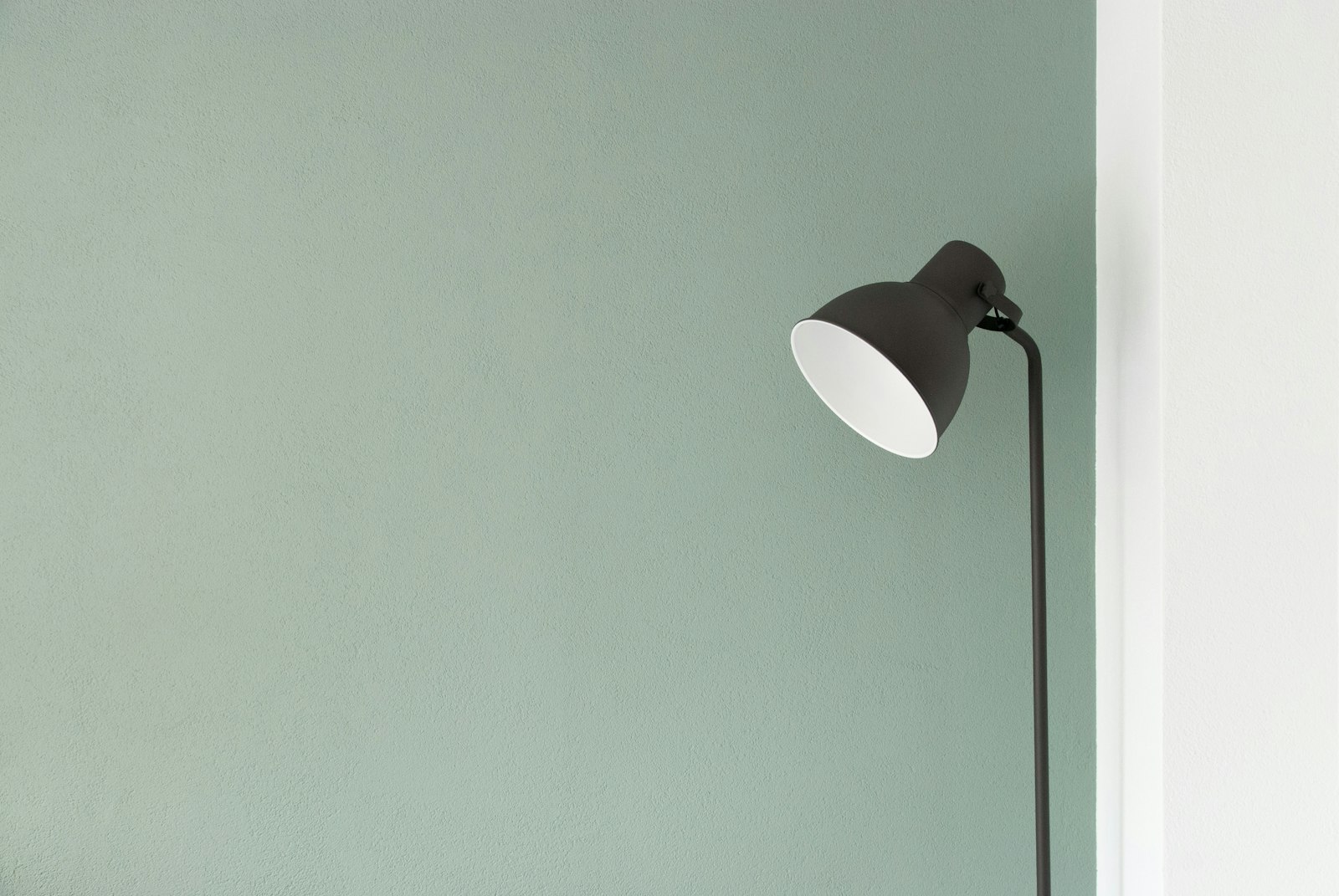 Black floor lamp angled against a sage green wall beside a white column