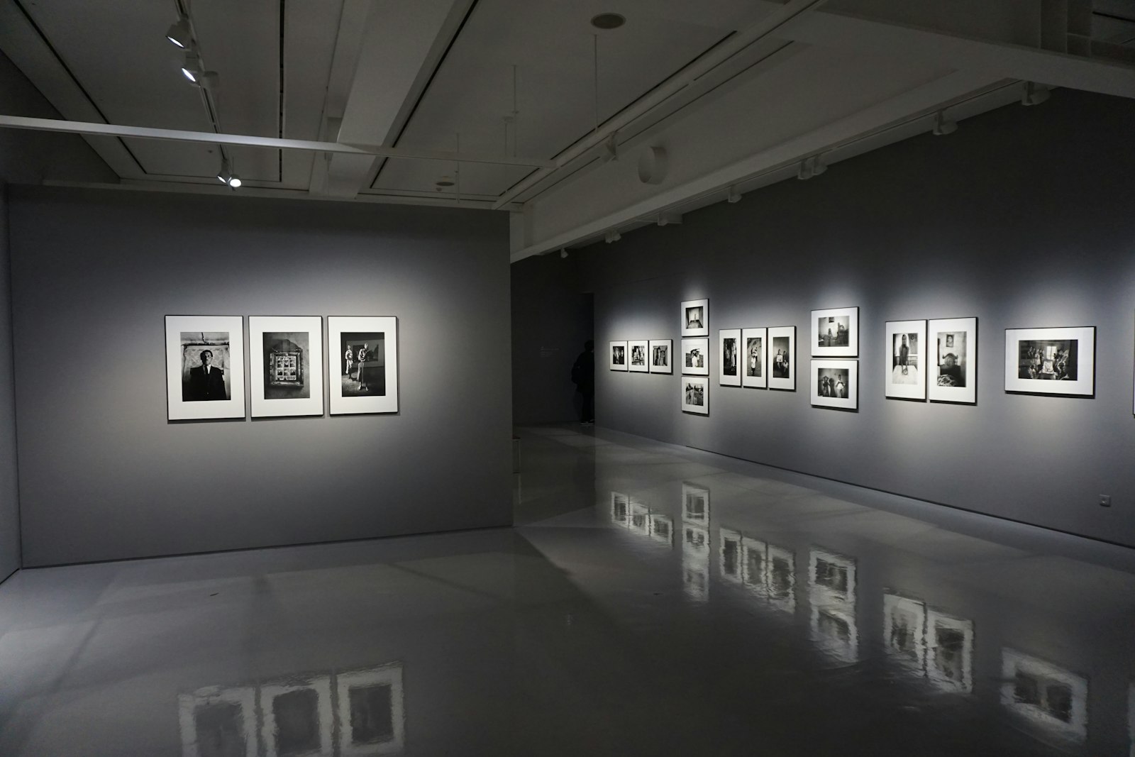 A dim gallery room with framed black and white photographs under spotlights