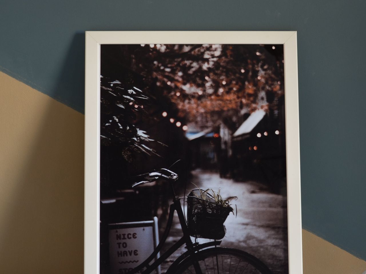 A framed print leaning against a teal wall on a wooden floor