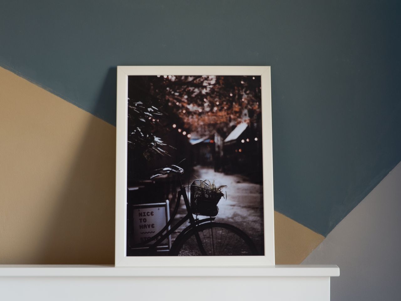 A framed print resting on a shelf against a teal and tan wall
